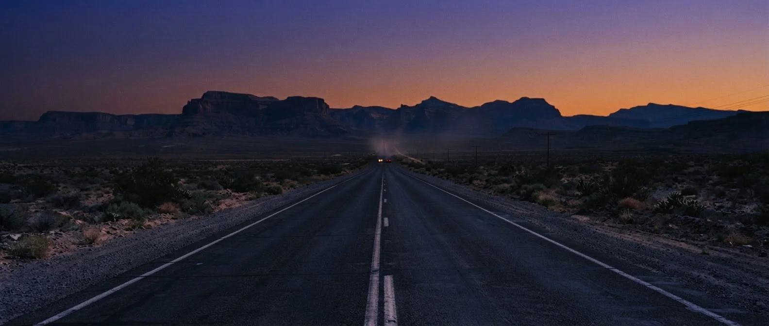grade this like a film still at dusk, deep purple and orange sky, long shadows, faint car headlights far down the road, keep the highway, mesas and framing